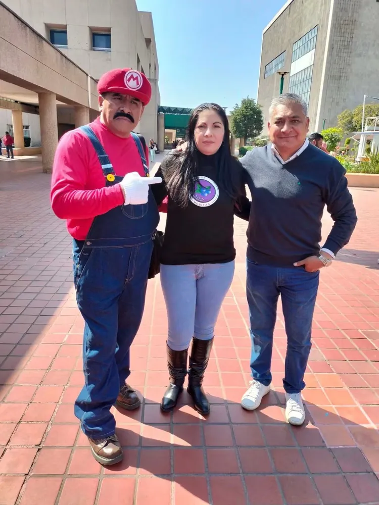 Tres personas posan en un evento, una de ellas con disfraz de Mario