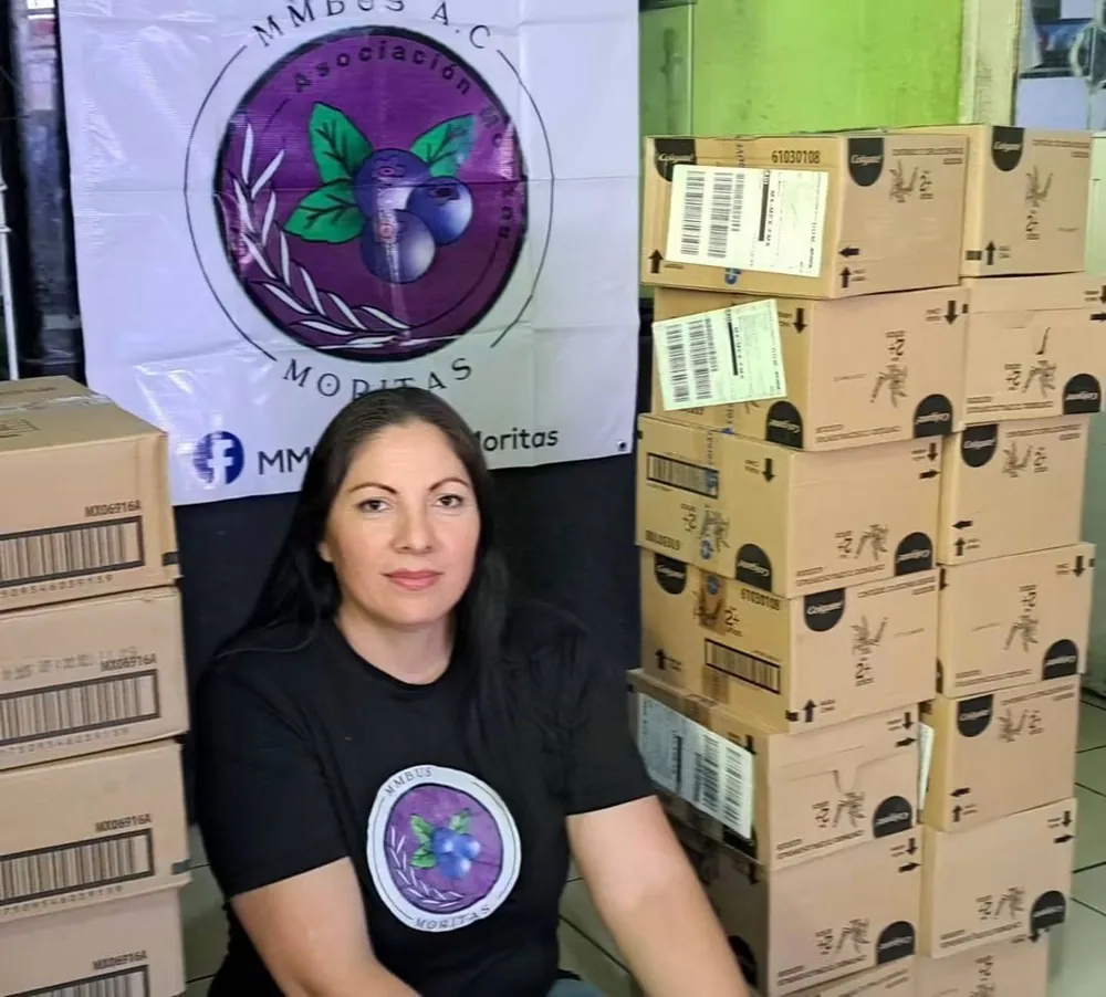 Integrante de la fundación junto a cajas de donativos y la lona de Moritas