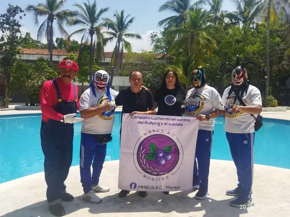 Luchadores y equipo con la lona de la campaña junto a una alberca
