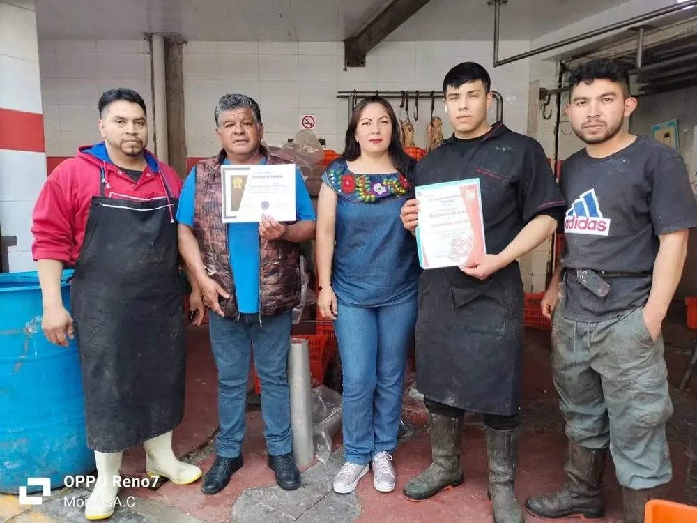 Grupo con delantales de trabajo muestra constancias de reconocimiento