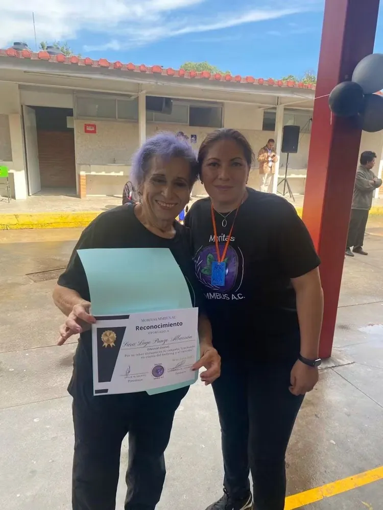 Dos mujeres sostienen una constancia en el patio de una escuela