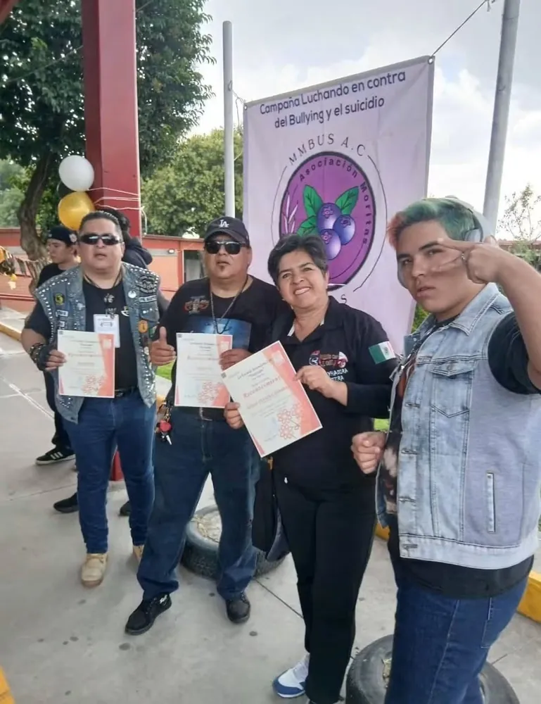 Grupo con constancias frente a la lona de la campaña contra el bullying