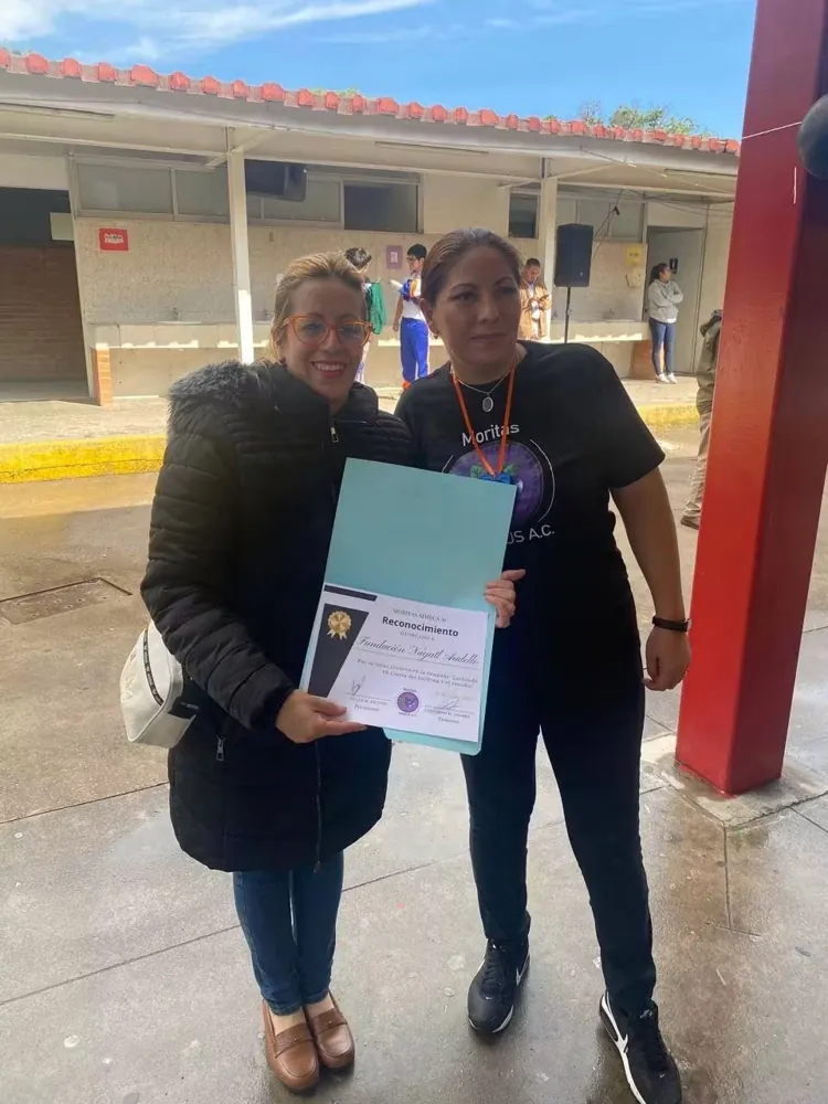 Integrante de la fundación recibe una constancia en el patio escolar