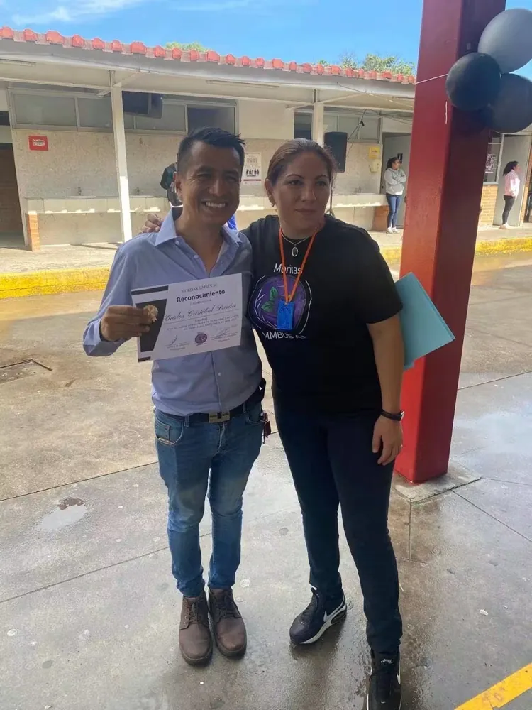 Dos personas posan con una constancia en una escuela