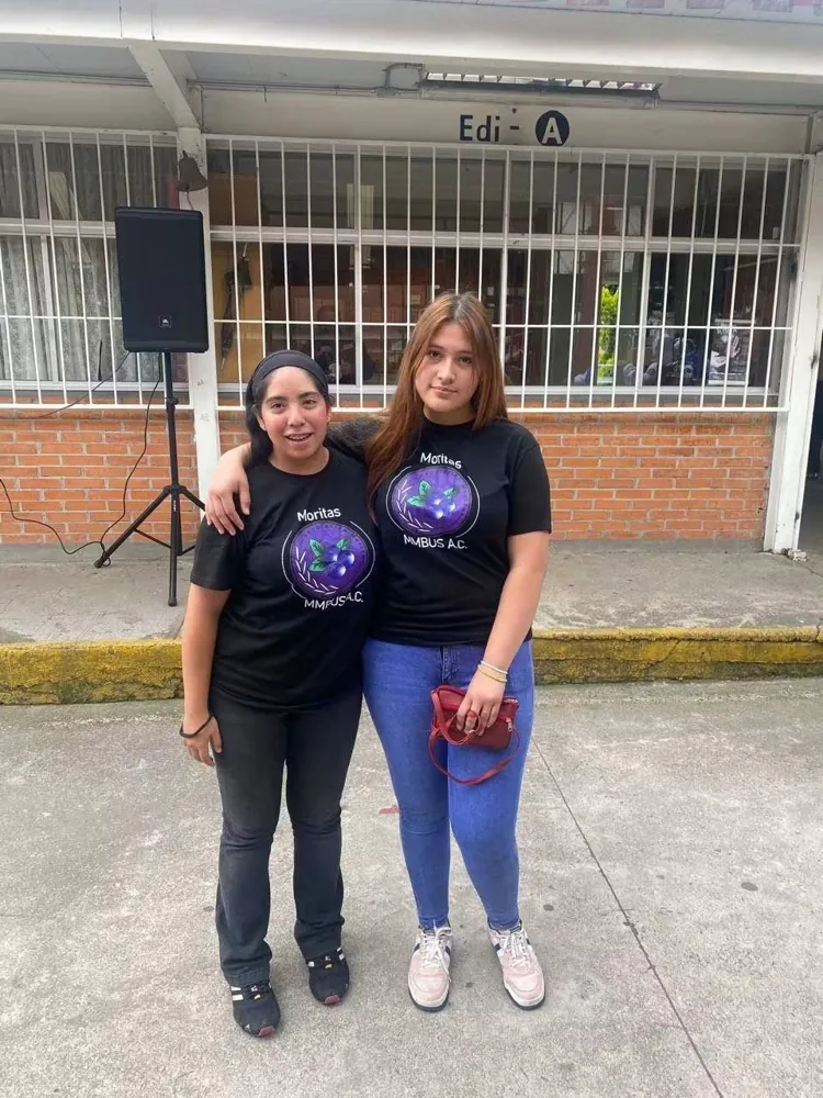 Dos integrantes del equipo posan frente a un edificio escolar